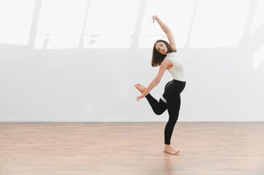 Parlak bir stüdyoda modern dans figürleri sergileyen zarif bir dansçı. Esneklik ve sanatsal ifade sergiliyor.