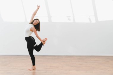 Ahşap zemin ve beyaz duvarları olan parlak bir stüdyoda çağdaş dans koreografisi uygulayan kadın dansçı.