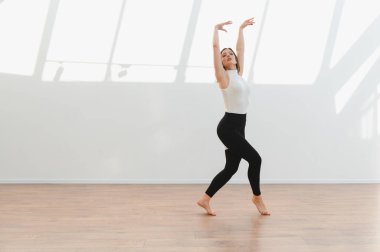 Güneşli bir stüdyoda modern bale hareketleri yapan zarif bir dansçı, esneklik ve sanatsal ifade sergiliyor.