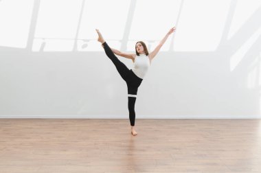 Dans öğrencisi, ahşap zemin ve beyaz duvarları olan parlak bir stüdyoda modern bir bale koreografisi uyguluyor.