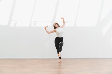 Geniş bir stüdyoda modern bir dans gösterisi sergileyen zarif dansçı esnekliğini ve sanatsal ifadesini sergiliyor.