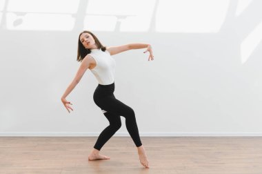 Dans öğrencisi parlak bir stüdyoda dans figürleri yapıyor. Parlak ahşap zeminde zarafet ve zarafet sergiliyor.