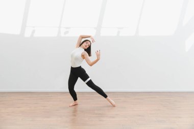 Parlak bir stüdyoda modern koreografi pratiği yapan kadın dansçı, parlak ahşap zeminde zarafet ve zarafet sergiliyor.