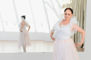 Beyaz etekli yaşlı balerin dans stüdyosunda bale hareketleri yapıyor. Zarafet ve adanmışlığı yansıtıyor.