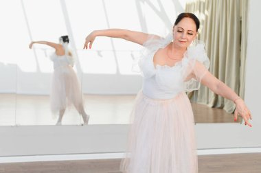 Yaşlı balerin parlak bir stüdyoda büyük bir aynaya yansıyan beyaz bir mayo ve pembe bir etek giyerek zarif bir şekilde dans eder.