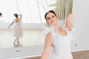 Zarif, olgun balerin zarif bir şekilde bir dans stüdyosunda bale pozu veriyor, arka planda yansıması yansıyor.