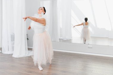 Zarif baş balerin, parlak bir dans stüdyosunda bale adımları çalışıyor. Yansıması duruşunu yansıtıyor ve sanata olan bağlılığını yansıtıyor.