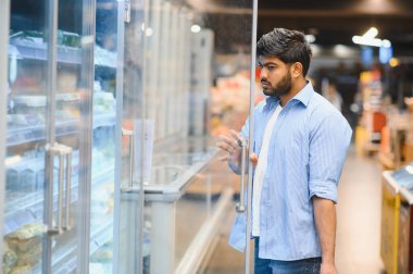 Odaklanmış müşteri buzdolabı kapısını açıyor, süpermarketin dondurulmuş gıda bölümünde bakkaliye arıyor.