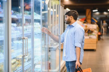 Müşteri buzdolabının kapısını açıyor, markette dondurulmuş yiyecek seçiyor, market alışverişi yapıyor.