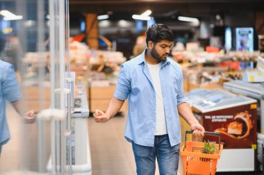 Bakkalda dondurulmuş ürünleri seçen, ananaslı alışveriş sepeti tutan, odaklanmış bir müşteri.