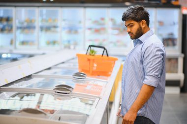 Genç Hintli bir adam market koridorunda dondurulmuş gıda ürünleri seçiyor.