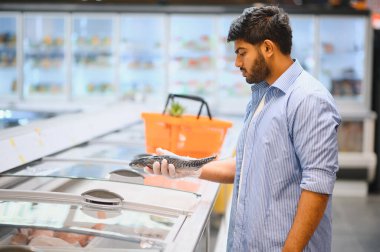 Plastik eldiven giyen genç Hintli adam marketten dondurulmuş balık seçiyor.