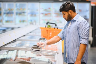 Plastik eldiven takan odaklanmış müşteri marketteki dondurulmuş ürünleri seçiyor.