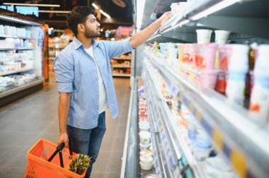Müşteri dondurulmuş raflardan süt ürünleri seçiyor, ananaslı alışveriş sepeti tutuyor, süpermarketten alışveriş yapıyor.