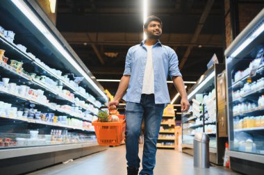 Parlak, düzenli bir süpermarkette alışveriş yaparken bir sepet taşıyan müşteri taze ürünler ve süt ürünleri seçiyor.