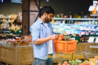 Genç Hintli müşteri marketten domates alıyor, elinde bir sepet tutuyor ve taze ürünler seçiyor.