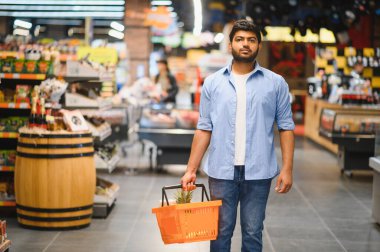 Bir marketin koridorlarında yürürken alışveriş sepeti taşıyan genç Hintli adam, yiyecek satın alıyor.