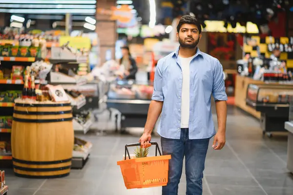 Bir marketin koridorlarında yürürken alışveriş sepeti taşıyan genç Hintli adam, yiyecek satın alıyor.