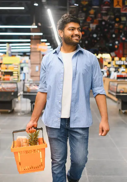 Parlak ve modern bir süpermarket koridorunda yürürken elinde alışveriş sepeti taşıyan gülümseyen genç Hintli adam çeşitli taze ürünlerin tadını çıkarıyor.