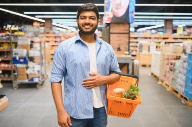 Markette yürürken alışveriş sepeti taşıyan genç Hintli adam.