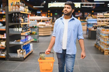 Market koridorunda yürürken alışveriş sepeti taşıyan müşteri ürünleri seçiyor.