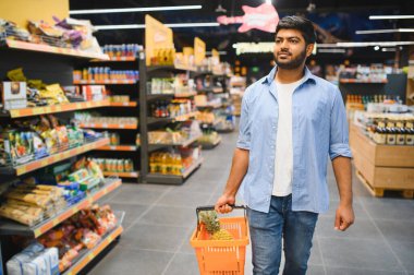 Market koridorlarında yürürken elinde ananasla alışveriş sepeti taşıyan genç Hintli bir adam.