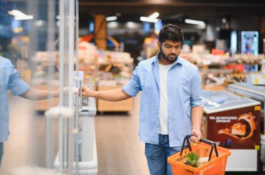 Odaklanmış müşteri süpermarkette alışveriş sepeti taşırken soğutulmuş bölüm kapısını açıyor