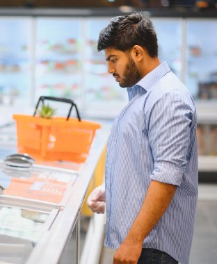 Market alışverişi yapan genç Hintli adam plastik eldiven giyerken süpermarketten dondurulmuş yiyecek seçiyor.