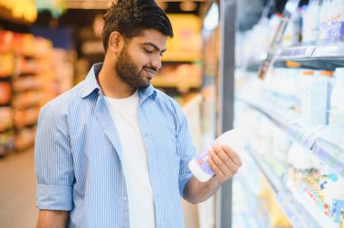 Genç Hintli adam süt şişesi etiketini okuyor, mandıra reyonunda satın alma kararı veriyor.