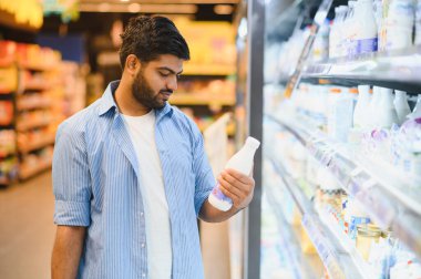Odaklanmış müşteri süt şişesi etiketini okuyor, mandıra koridorunda satın alma kararı veriyor.