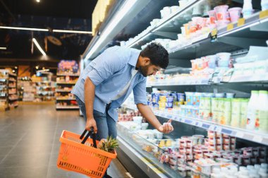 Müşteri alışveriş sepetini tutuyor ve süpermarketin soğutulmuş bölümünden yiyecek seçiyor.