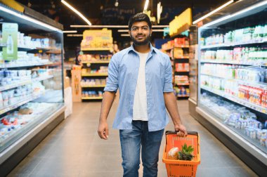 Markette yürüyen, içi taze yiyecek ve sebzelerle dolu bir alışveriş sepeti taşıyan mutlu Hintli müşteri, alışveriş deneyiminin tadını çıkarıyor.