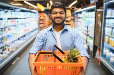 Alışveriş sepetini elinde tutan genç Hintli bir adam markette gülümsüyor ve yürüyordu.