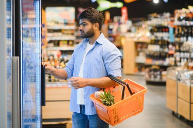 Müşteri buzdolabının kapısını açıyor, süpermarkette alışveriş sepeti tutuyor, gıda ürünlerini seçiyor, market alışverişi yapıyor.