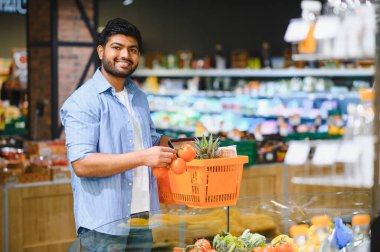 Markette olgun domatesleri seçerken elinde bir alışveriş sepeti tutan müşteri canlı taze ürünlerin keyfini çıkarıyor.