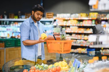 Genç Hintli adam taze sebze seçiyor ve markette alışveriş yaparken elinde sarı dolma biber tutuyor.