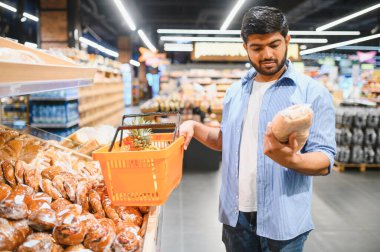 Genç adam ekmek almak için alışveriş yapıyor ve süpermarketin fırın bölümünde ananaslı bir sepet tutuyor.