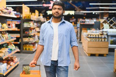 Market koridorlarında yürürken ananasla alışveriş sepeti taşıyan odaklanmış Hintli müşteri