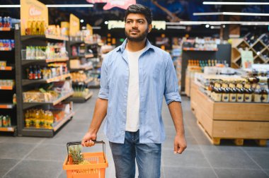 İçi ananas dolu alışveriş sepetiyle süpermarkette yürüyen genç Hintli adam, ürünleri seçiyor.