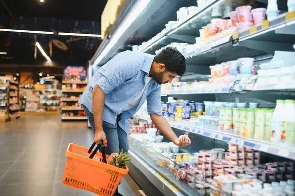 Müşteri alışveriş sepetini tutuyor ve süpermarketin soğutulmuş bölümünden yiyecek seçiyor.