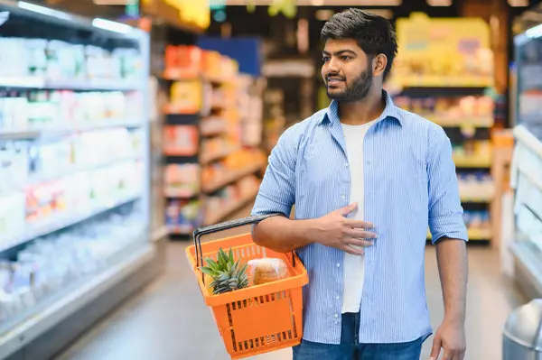Markette yürürken ve ürünleri seçerken elinde alışveriş sepeti taşıyan genç Hintli bir adam.