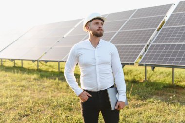 Erkek mühendis, güneş panelleriyle sahada duruyor ve elinde dizüstü bilgisayar var. Yenilenebilir enerji kavramı