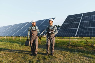 Açık hava yenilenebilir enerji santralinde birçok fotovoltaik paneli olan yeni enerji projelerini yürüten ve tartışan mühendisler