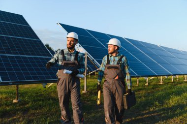 Güneş panellerini inceleyip sürdürülebilir bir enerji santralinin planlarını tartışan iki mühendis.