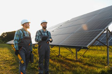 Gün batımında güneş panellerini denetleyen sabit şapkalı mühendisler, sürdürülebilir gelecek için yenilenebilir enerji üretiyorlar.