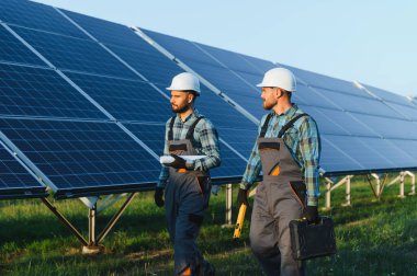 Bir güneş paneli dizisinde yürüyen iki işçi, bakım yapıyor ve verimli enerji üretimini sağlıyorlar.