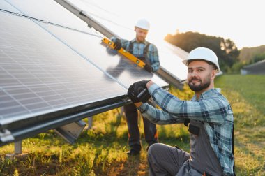 Güneş panellerini yenilenebilir enerji sistemine bağlayan teknisyenler. Takım çalışması ve sürdürülebilir güç üretimi vurgulanıyor