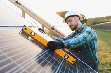 Solar panellerin yenilenebilir enerji için hassas kurulumunu sağlayan bir seviye aracıyla hizalanmasını denetleyen sert başlık işçisi