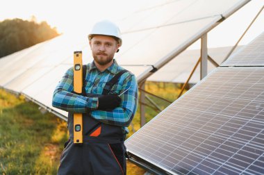 Erkek teknisyen, günbatımında temiz yenilenebilir enerji üreten güneş panelleri üzerinde çalışıyor.