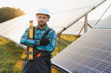 Erkek mühendis, başlık ve tulum takıyor. Güneş panelinde ruh seviyesini koruyor. Yenilenebilir enerjiye odaklanıyor.